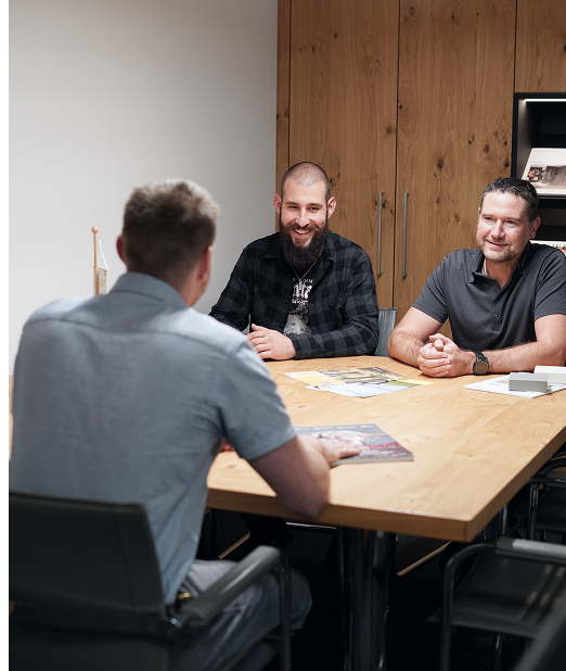 Drei Männer sitzen an einem Besprechungstisch und führen ein Gespräch in einem modernen Büro.