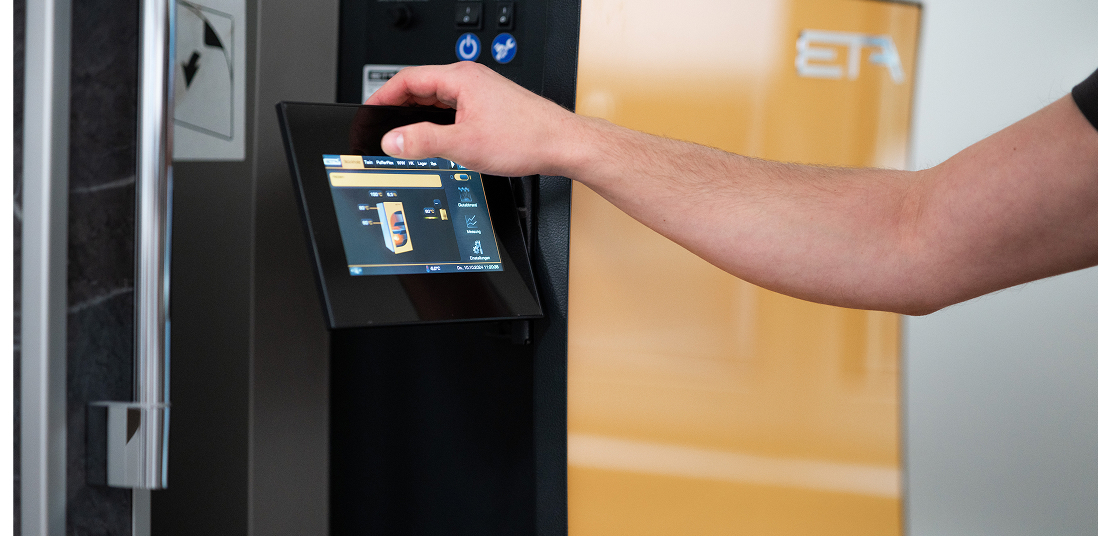 Eine Person bedient über einen Touchscreen die Steuerung einer modernen Heizungsanlage der Marke ETA.