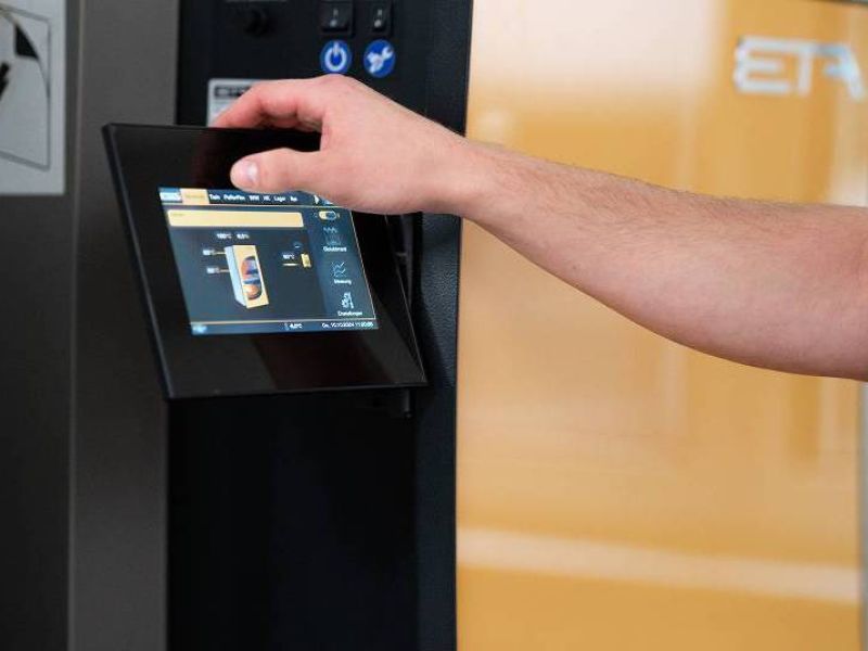 Eine Person bedient über einen Touchscreen die Steuerung einer modernen Heizungsanlage der Marke ETA.