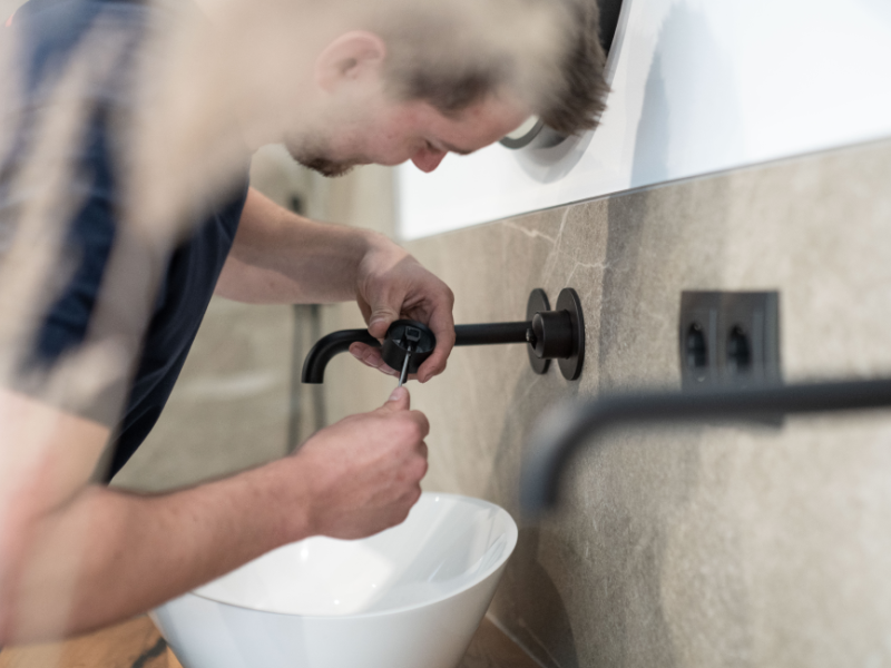 Mann repariert im Badezimmer eine Wasserleitung